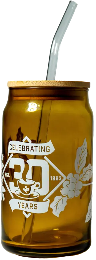 Ein bernsteinfarbenes, dosenförmiges Glas mit dem Aufdruck „Celebrating Thirty Years“ auf der Seite.  Auf der Seite sind außerdem Kaffeepflanzen und eine Kaffeetasse aufgedruckt.  Das Glas hat einen einfachen Bambusdeckel und einen klaren Glasstrohhalm.