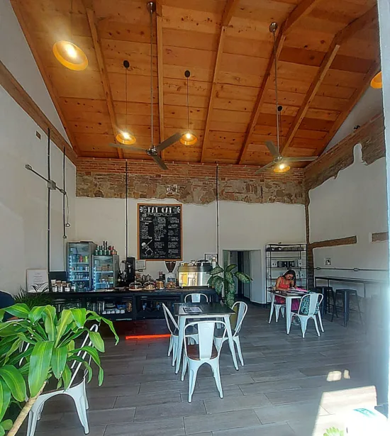 Inside Fat Cat, there are tall wooden ceilings with hanging fans, plants, a black coffee bar with pastries set out and some exposed brick along the walls.