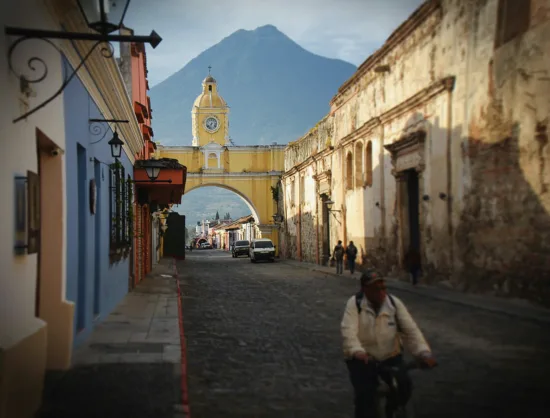 a colorful street in Antigua with a mountain in the background and a man on a bicycle.