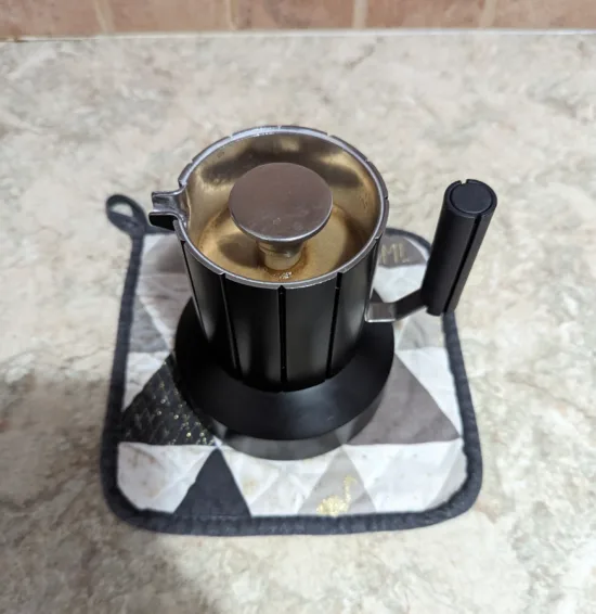 Moka pot on a trivet, brewing coffee.