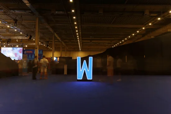 A large W lit with blue light in a mostly empty hall at World of Coffee.