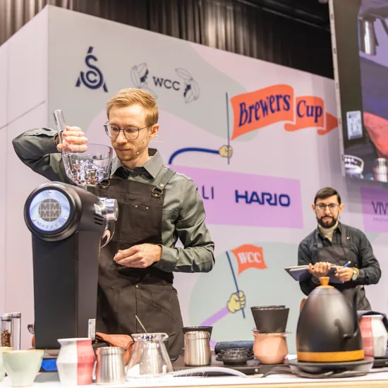 Martin grinds beans on stage as a judge looks on and takes notes.