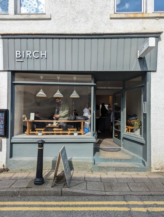 Outside Birch, the exterior is wood paneled in a blue-gray color, with big windows, plants and pendant lights visible inside.