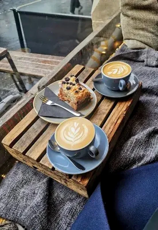 A small wood tray with a cappucino and latte cup, and a blueberry cake or scone.