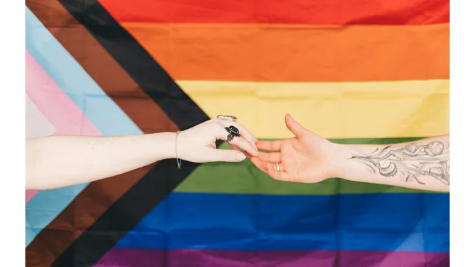 Two hands join in front of a Pride flag