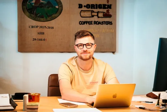 Michael sits at his desk. He wears a D Origen t-shirt and glasses.