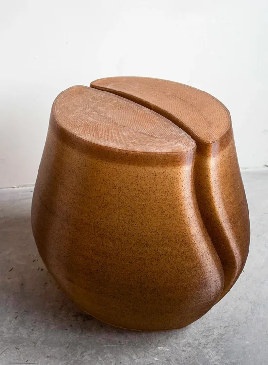 A stool shaped like a coffee bean, flat on top with a rivet in the middle and a bulbous shape.