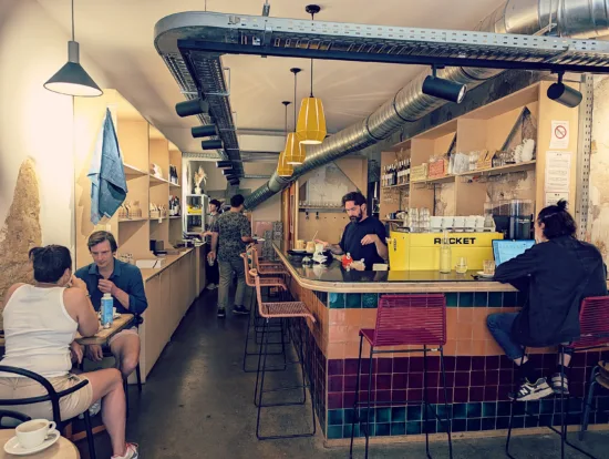 Inside Mana, with yellow pendant lights, tall barstools, a yellow espresso machine, and tile bar.