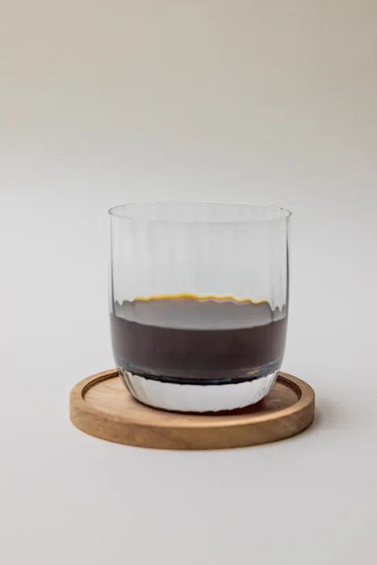 A glass of cold coffee on a round wooden coaster.