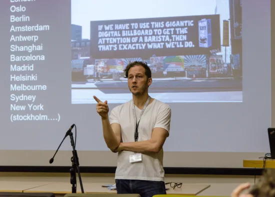 A speaker wearing a lanyard addresses an audience.