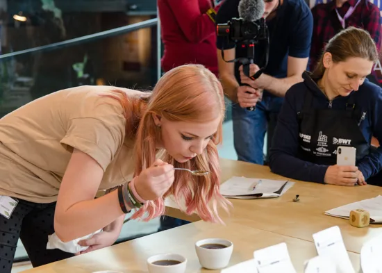 A barista blows on coffee in a cupping spoon during a tasting.