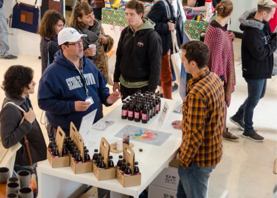 People talk over bottled coffee at a booth.