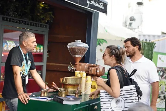 Two people speak to a man at a booth  with a coffee grinder.