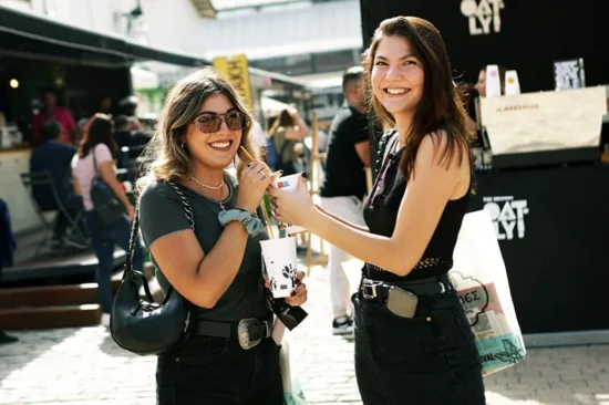 Two women with coffee cups smile outside an Oatly booth.