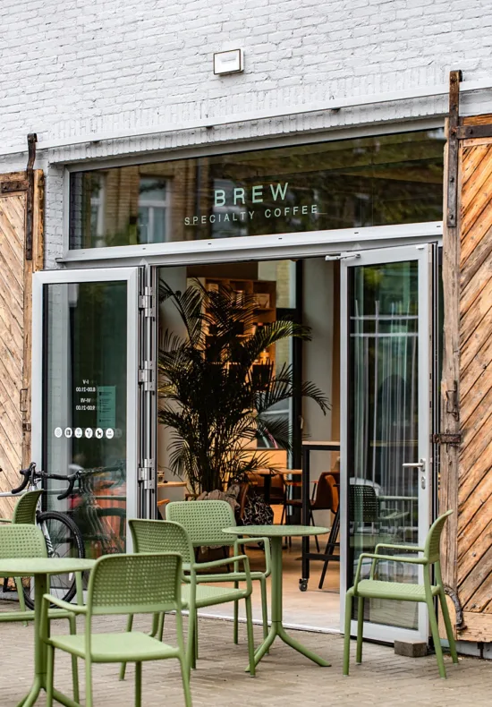 Green tables and chairs outside the tropical themed Brew, which has a palm tree inside the door.