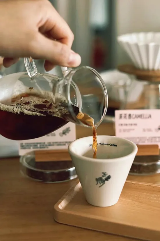 Coffee is being poured from a glass carafe into a white coffee cup.