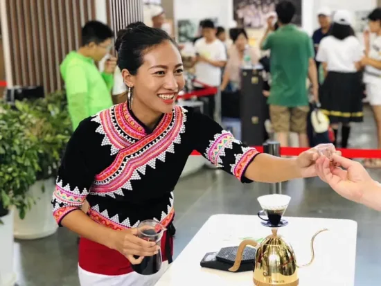 Zhao Mei hands a coffee sample to someone from a booth at a trade show.