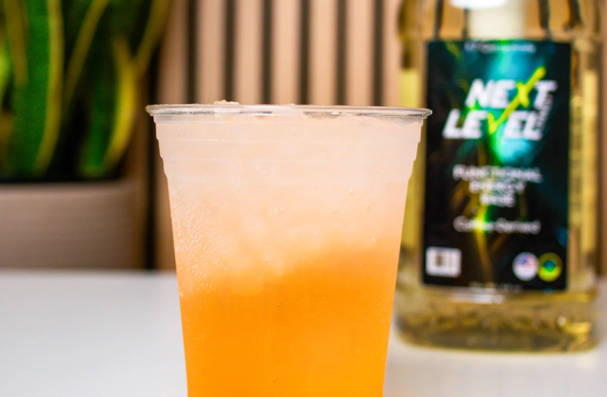 A Peach Mango Sunrise Refresher in a plastic cup on a counter with a Next Level bottle behind it.