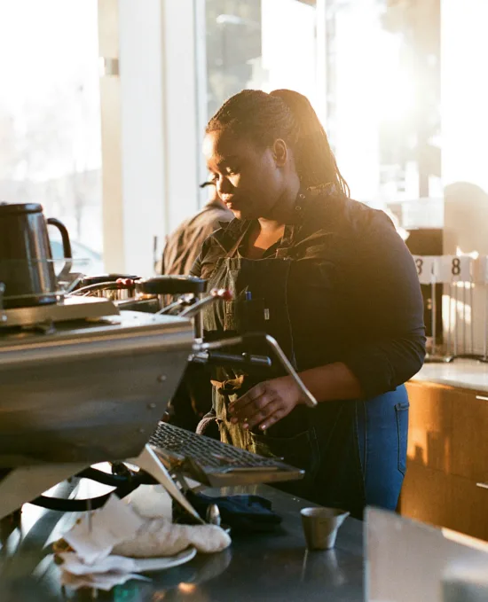 A barista works the espresso machine, another works behind them.