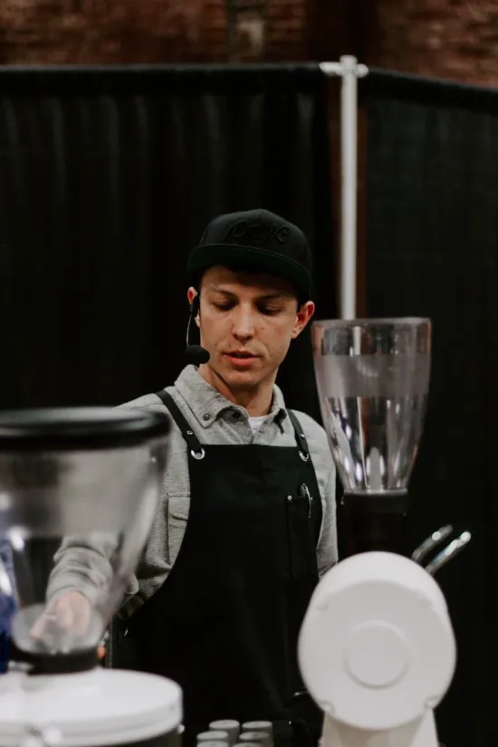 Dylan with a microphone on stage behind coffee equipment.