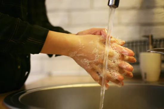 A person washes their hands with soap in a steel sink.