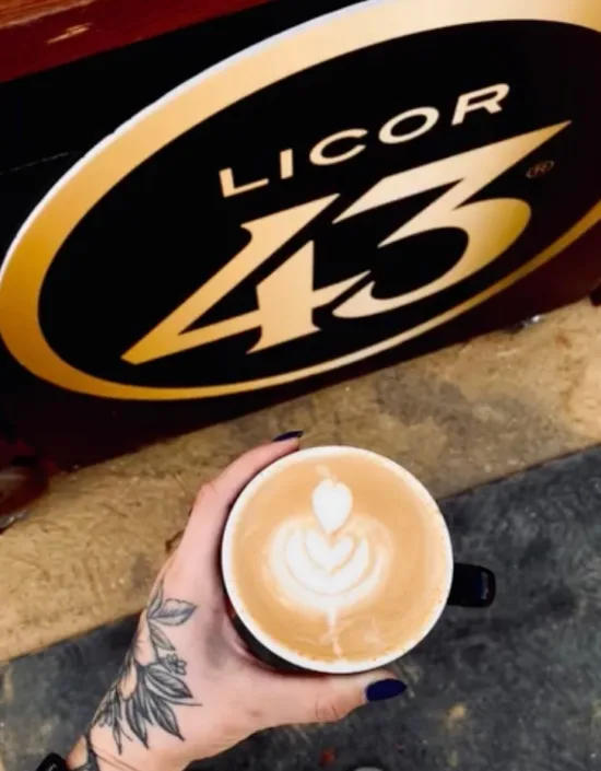 A hand holds a cup with latte art poured in it by a Licor 43 sign at the Bartender & Barista Challenge.