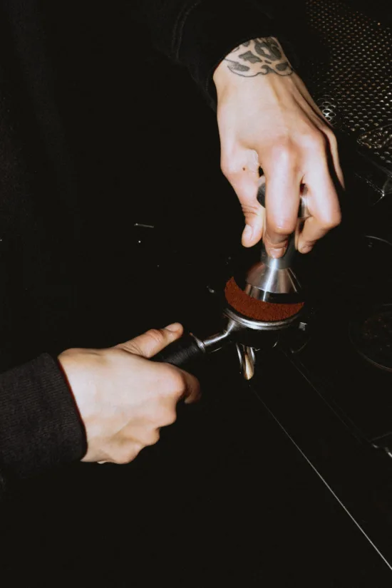 A barista tamping an espresso shot in a closeup of a portafilter.