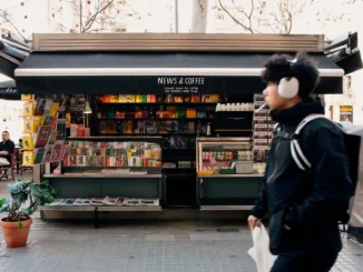 A passerby in headphones walks in front of News & Coffee stand.