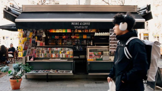 A passerby in headphones walks in front of News & Coffee stand.