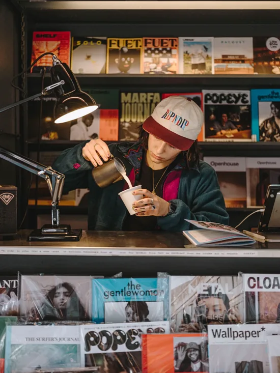 A barista at News & Coffee pours milk into a coffee cup.