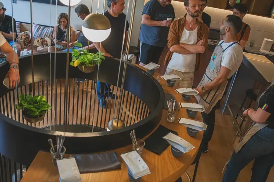 A circular table holds coffee bags, cupping spoons, and brews for a tasting.