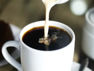 Milk being poured into a white mug of hot coffee.