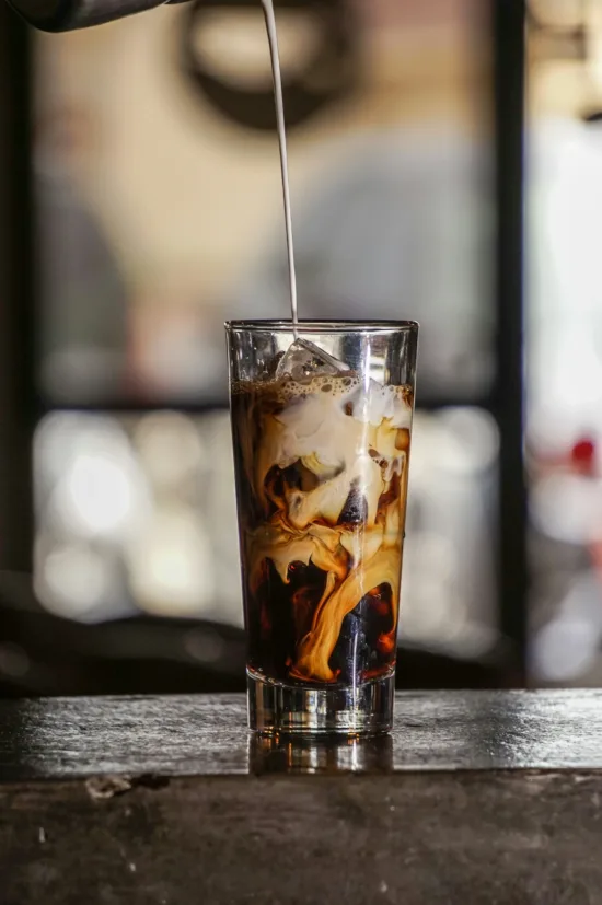 Iced coffee glass with milk being poured in the top.