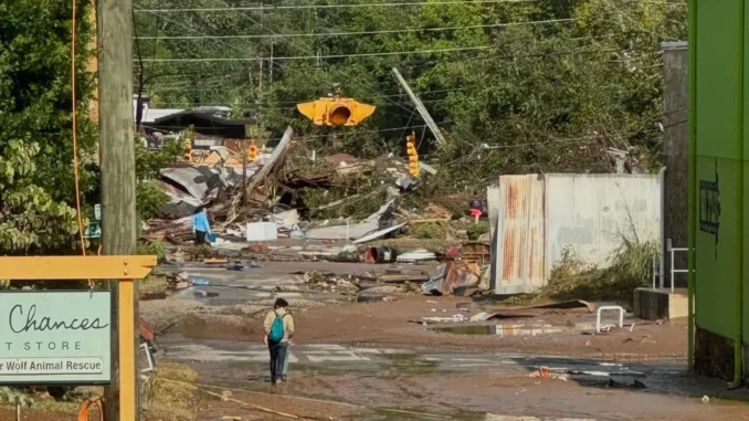 Devastated buildings and shrapnel in NC. A person walks through the mud.