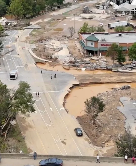 Devastation from Helene: crumpled buildings, flood waters, & washed out road.