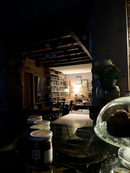 Inside a dark café, with rows of books and jars, tables, flowers, and a cake stand.