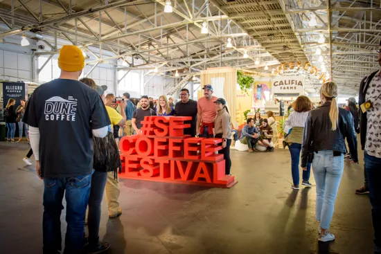 People gather for a photo around the giant #SFCOFFEEFESTIVAL statue in big red letters.