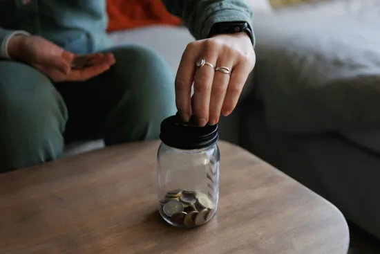 A hand putting loose change in a glass jar.