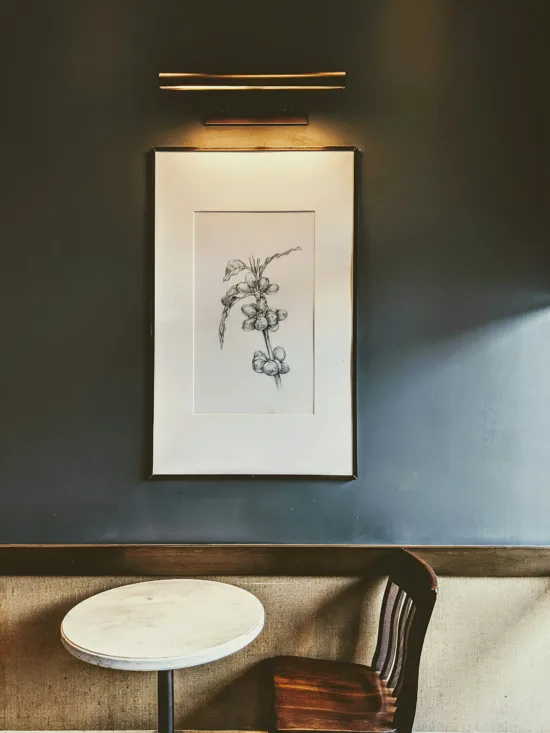 A drawing of a coffee plant stalk framed on a shop wall above a small table and chair.