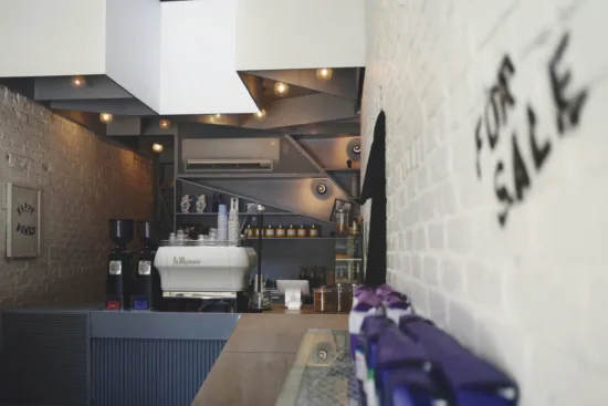 Inside an empty café. An espresso machine is in front of the back wall, while coffee bags are for sale to the right.